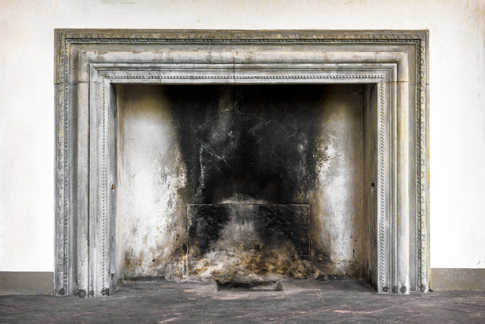 An old fireplace with mold. Very rundown and full of soot. Surrounded by an old dirty wooden mantel. 